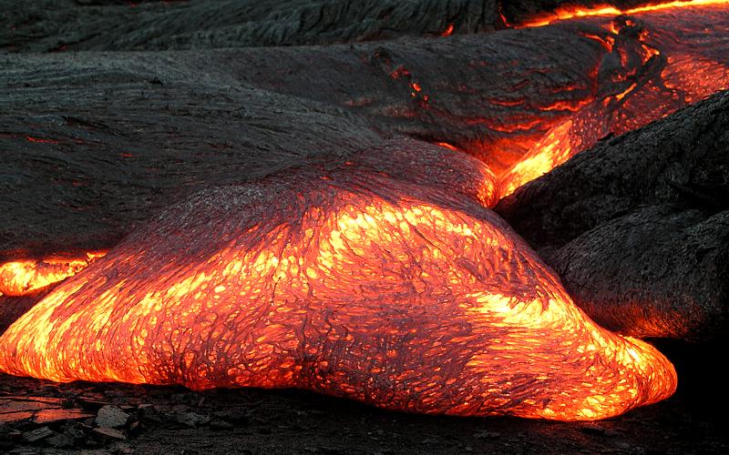 This brilliantly glowing hump of magma is evocatively called "Pahoehoe's Toe". Dark reds and oranges shade to a bright yellow toward the top of the hump. There, the colors quickly transition through red to dark gray as the lump cools from the top down.